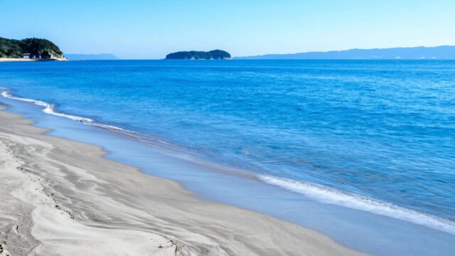 初夏の朝、瀬戸内海の砂浜と波打ち際をやや高い位置から見下ろした中景。人物のいない釣り場の風景