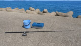 堤防に置かれた泳がせ釣り用の竿と水汲みバケツのある釣り座