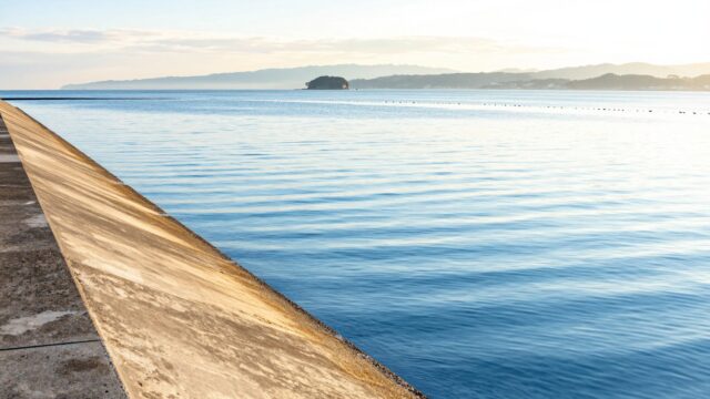 朝の光に照らされた瀬戸内の防波堤と、遠くの島影まで見渡せる穏やかな海面