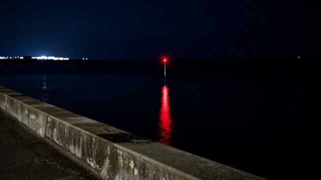 夜の堤防から見た、海面に浮かぶ電気ウキの赤い明かり