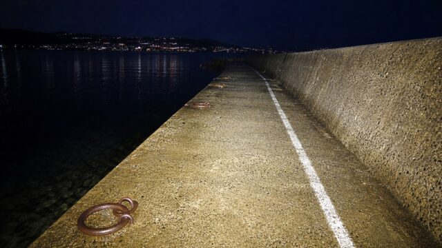 ヘッドライトの光で堤防の路面と白線が前方まで明るく照らし出されている夜の情景