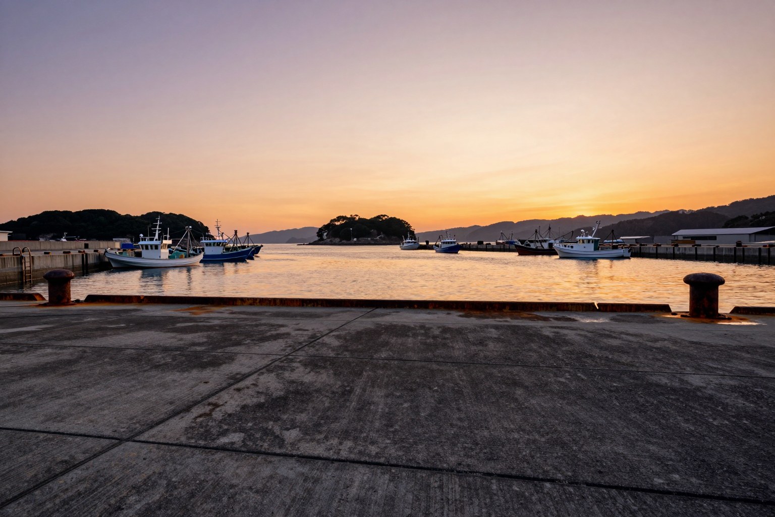 夕方の瀬戸内の港。護岸のコンクリート面すれすれのローアングルから、係留された小型船と静かな水面を見渡した引きの風景