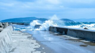 風の強い日の瀬戸内の堤防。白波の立つ海から波しぶきが上がり、誰もいない岸壁を低い位置から広く引いて写した写真
