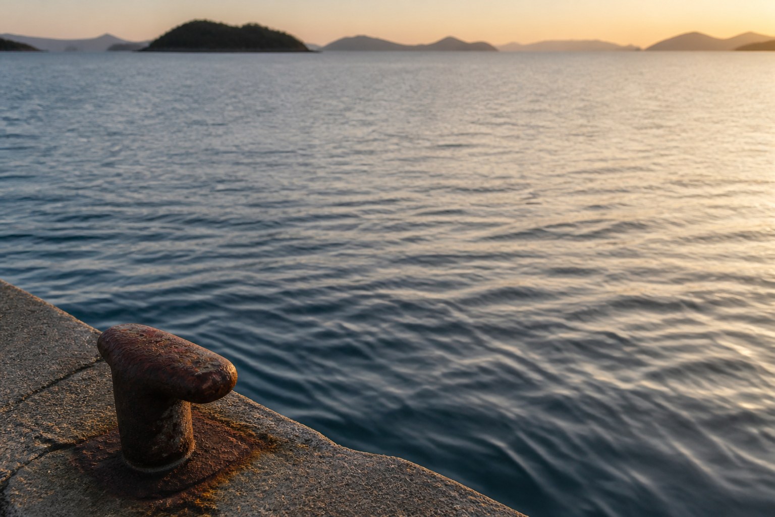 冬の夕方の瀬戸内。穏やかな海面に低い夕日が反射し、手前に岸壁の縁が入る誰もいない釣り場を、やや高い位置から水面に寄って写した写真